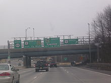 A multilane freeway with a set of four green signs over the road. The left sign reads north Route 440, the second sign reads U.S. Route 9 north Garden State Parkway exit 1/2 mile, the third sign reads Garden State Parkway south no trucks exit 1/4 mile, and the right sign reads U.S. Route 9 south with an arrow pointing to the upper right