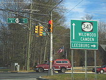 A road at a traffic light, with a green sign on the traffic light arm reading north up arrow Route 47 south right arrow. Another green sign on the right side of the road reads up arrow Route 347 Wildwood Camden Leesburg right arrow