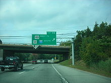 Ground-level view of a four-lane divided highway with a narrow grassy median separating the opposing lanes of traffic; signage for a square Route 401 and Route 2 shields are in view