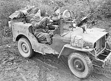 two men in a machine gun armed Jeep, the rear of the vehicle is overloaded with equipment