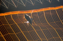 An image of a black and orange solar array, shown uneven and with a large tear visible towards its top edge. A scaffold-like structure is visible above the array.