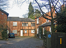 A cobbled courtyard with brick buildings on three sides, some of them timber-framed. On the gatepost on the right is a blue commemorative plaque
