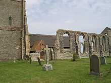 On the left the lower part of a tower, on the right the ruined wall of the aisle, and between them part of the small newer church with a thatched roof