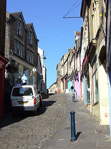 Street scene showing narrow cobbled road past coloured shop fronts