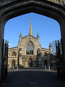 View through an archway of end of a church with a central door flanked by canopied niches containing statues. Arched window above the door and spire behind.