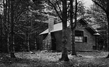 A cottage with a chimney stands in the woods.