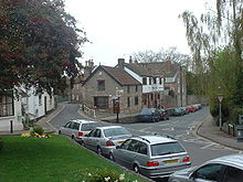 Street scene showing grass area to the left of road junction. Ahead are buildings.