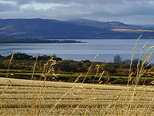  A view of stubble field, a body of water and dark hills beyond