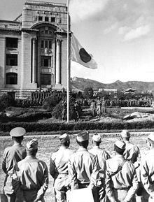 Men in military dress watch a flag being lowered.