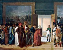 A group of men, some wearing beards and turbans, are in a room with a large painting on the wall, they look towards a doorway wear a man in military uniform including white johphurs (Napoleon) looks back at them and has his right hand in his waistcoat.