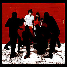 A male and female stand are pestered by black silhouettes in front of a brick wall on what appears to be snowy ground. A black border outlines the artwork. Dominant colors are red, black, and white.