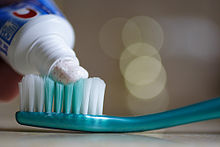 A tube applying toothpaste to a toothbrush.