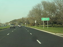 A six-lane divided highway approaching a traffic light. A green sign on the right side of the road reads Jamesburg Keep Right while a junction Route 32 shield can be seen in the distance