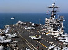 F/A-18 Hornet launches from the flight deck of USS Truman. Other aircraft are stored on deck.