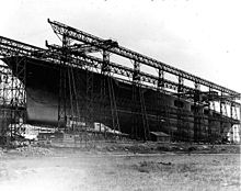 Large ship with no superstructure with scaffold-like steel surrounding her.