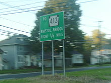A green sign in the median of a divided highway reading to Pennsylvania Route 413 Bristol Bridge right 1/4 mile