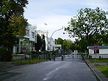 A street with a crossing green fence and a barrier with guard houses.