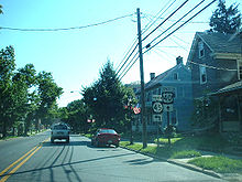 A two-lane road in a residential area with signs on the right side of the road reading north Route 45 left and east U.S. Route 40 straight