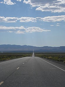 View across a desert valley with a highway proceeding straight for many miles towards the horizon and a distant mountain range