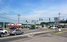 A signalized five-way intersection of three highways in an area composed of several commercial establishments.