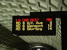 A electronic sign with multicolor text display mounted over a station platform.