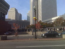 People waiting in line behind a fence in a city.