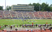 Football stadium with two teams on the field and stands full on sunny day