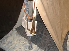 Bugle on leather strap hangs outside a small tent.