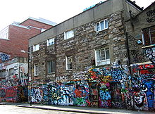 A three-storey stone-faced building. The first level is decorated with colorful graffiti.