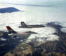 Two jet aircraft flying together over mountain range and cloud.