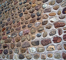A wall with many small round stones set in a brownish mortar, closer to white near the bottom right of the image