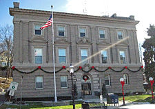 A three-story flat-roofed rectangular stone building with an American flag out front and Christmas decorations on the facade