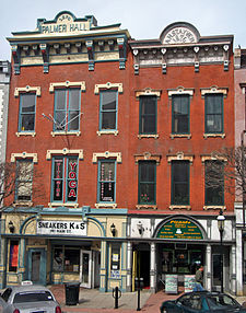 Two attached brick buildings three stories height with colorful, ornate detailing and storefronts at street level. The one on the left has "Sneakers K & S" on its storefront and "Palmer Hall" at the top. The one on the right has "Picante" at the storefront and "A.H. Stayver 1876" at the top.