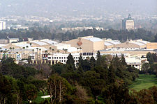 A photograph of a large set of buildings, behind several trees and a hill.
