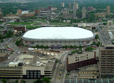 Stadium with a white domed roof surrounded by rail lines and other buildings