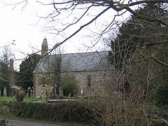 Stone building partially obscured by trees. In the foreground are gravestones.