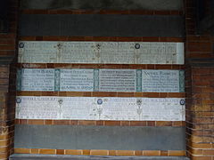 Memorial tablets arranged in three rows on a wall. Those in the centre are in the green and white Arts and Crafts Movement style, while those above and below are in the more recent design. There are empty rows above and below the three filled rows.