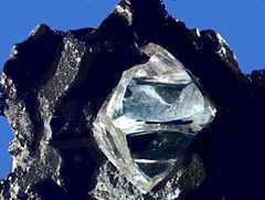 A clear octahedral stone protrudes from a black rock.
