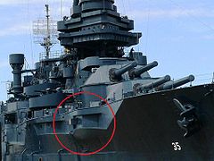 A permanently docked museum ship with a red circle on the photograph to highlight a gun protruding from an opening the in the ship's port side.