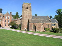 Reddish stone buildings. The church in the foreground has a square tower.