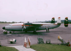 Twin-engine turboprop airliner with three fins parked on ramp while being serviced, with mobile staircases located nearby.