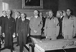 Interior photograph, showing in the foreground the five main signatories to the Munich Agreement, and in the background their various aides and assistants. Of the five, the two to the left are in black suits, the remainder in military uniform.