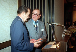 Two men stand at a podium as one hands a plaque to the other.