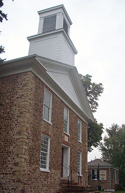 A brownish building made with small round stones topped with a white square wooden tower