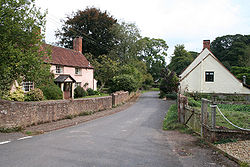 Street scene with houses and trees separated from the road by a stone wall.