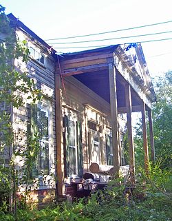 The overgrown front of a house in disrepair, with columns and a pediment