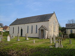 White painted building with arched windows. In the foreground are gravestones.