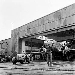 Twin-engined transport aircraft being towed from hangar by a tractor