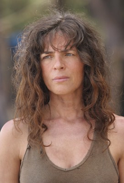 Head and shoulders of an attractive middle aged woman with long curly brown hair, wearing a brown tank top, with a sad frown on her face.