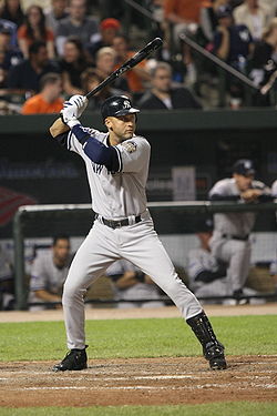 A man in a grey baseball uniform with a navy helmet prepares to swing at a pitch